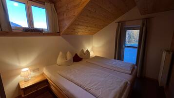 A bedroom with a wooden ceiling, a bed with white bedding, a bedside table with a lamp, and a window with curtains.
