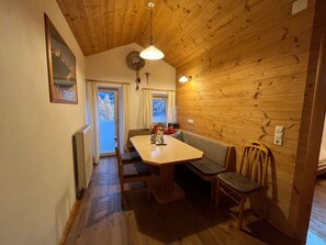 A cozy room with a wooden ceiling, a dining table with chairs, a bench, a window with curtains, and a wall-mounted light fixture. - Apartment Enzian - Innerkratzerhof **** 4 apartments (Bichl)