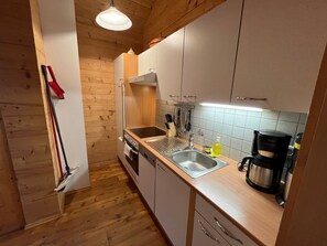 Una cocina compacta con armarios de madera, un lavamanos de acero inoxidable y una cafetera.
