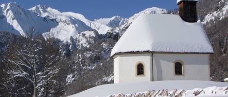 A snow-covered church with a bell tower, surrounded by mountains and trees.