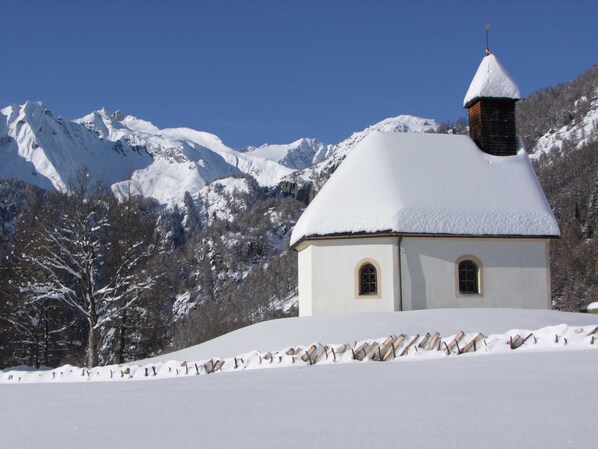 A snow-covered church with a bell tower, surrounded by mountains and trees.