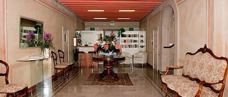 Hall dell'hotel con reception, area salotto e scaffali di libri.
