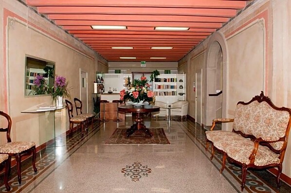 A hotel lobby with a reception desk, seating area, and bookshelves.