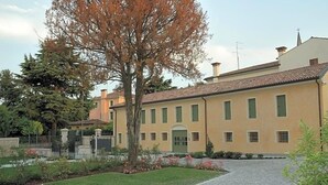 Un edificio de dos pisos con fachada simétrica, entrada central y un jardín con diversas plantas y flores.
