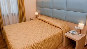 Una habitación de hotel con cama, mesita de noche, lámpara y teléfono.
