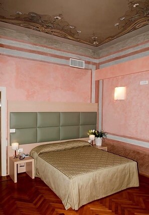 A bedroom with a large bed, a nightstand with a lamp, and a wall-mounted light fixture.