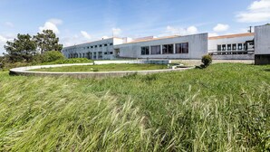 A modern building with a flat roof, large windows, and a grassy area in front. - HI Almograve - Pousada de Juventude - Hostel (Odemira)