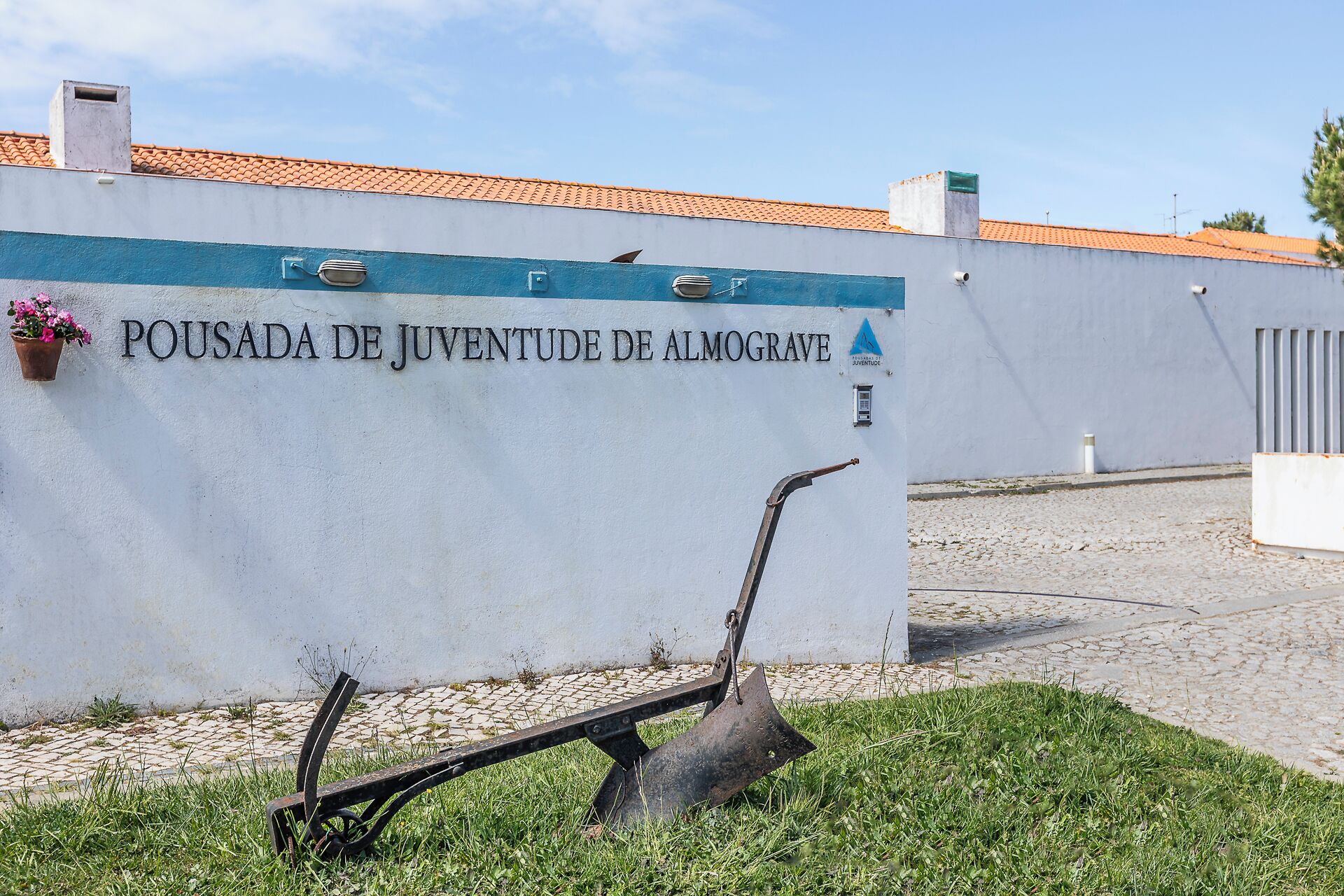 Un cartel que dice 'POUSADA DE JUVENTUDE DE ALMOGRADE' con una pala de metal al frente.