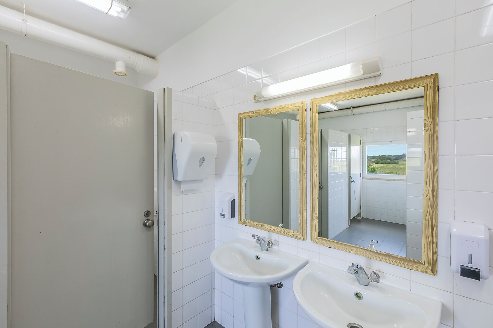 A bathroom with two sinks, a mirror with a wooden frame, and a window with a view of the outdoors.