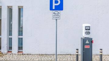 A parking sign with electric vehicle charging symbol, a charging station, and a building with large windows.