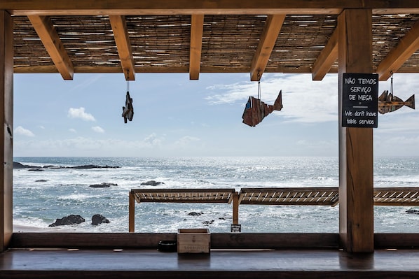 Una estructura de madera con vista al océano, un letrero que indica que no hay servicio de mesas y un banco.