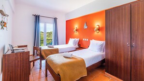 A hotel room with two beds, a desk with a laptop, a chair, and a view of greenery outside. - HI Almograve - Pousada de Juventude - Hostel (Odemira)