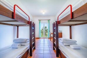 A room with two bunk beds, a wooden floor, a window with curtains, and a view of trees outside.