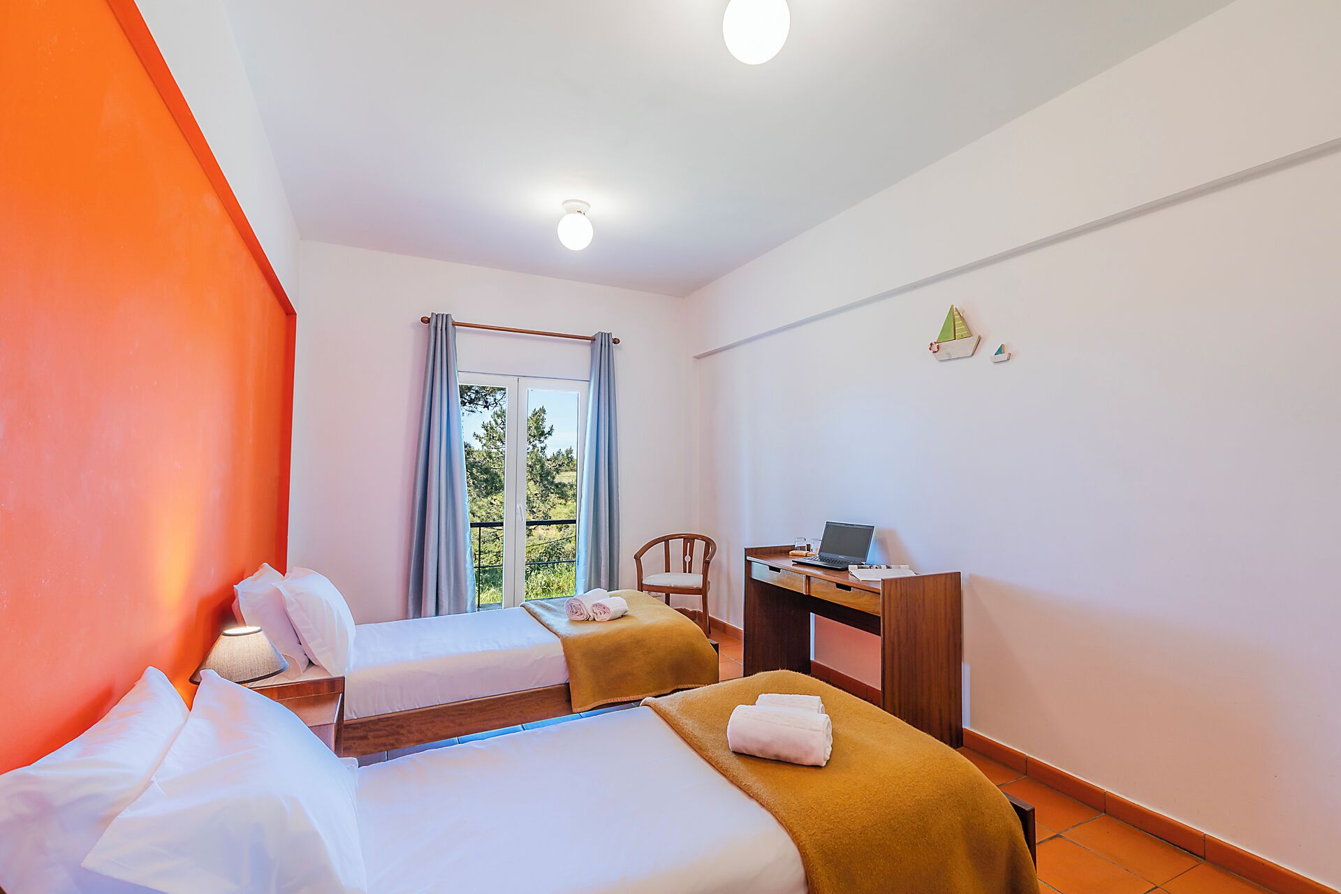 A hotel room with two beds, a desk with a laptop, a chair, and a window with curtains.
