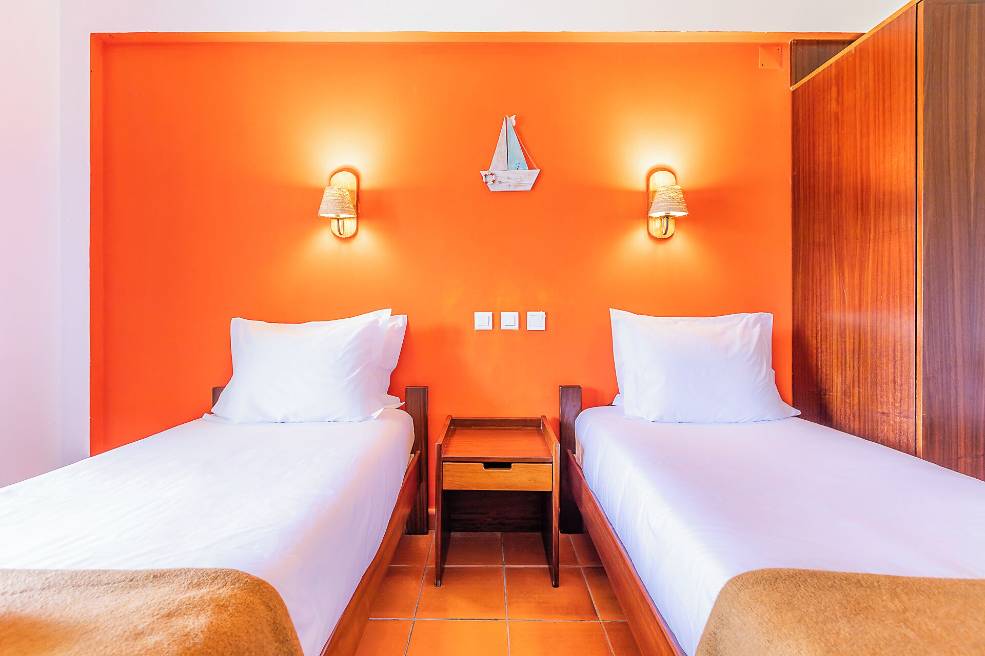 A hotel room with two beds, a nightstand, and a wall-mounted light fixture.