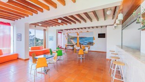 A spacious room with a high ceiling, wooden beams, orange seating, and a large window with a view. - HI Almograve - Pousada de Juventude - Hostel (Odemira)