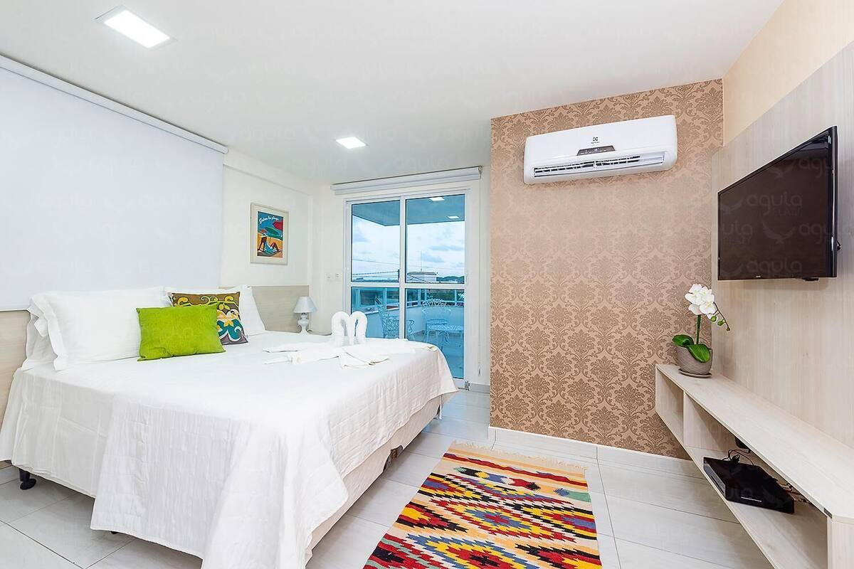 Habitación de hotel con cama, televisión, aire acondicionado instalado en la pared, ventana y balcón.