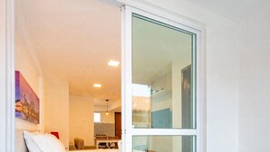 A hotel room with a bed, a wooden table, and a glass door leading to a balcony. - Aguia Flats (Natal)