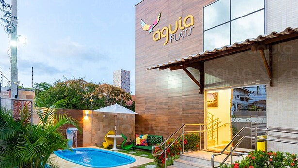 A modern building with a swimming pool, outdoor seating, and a well-maintained garden. - Aguia Flats (Natal)