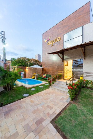 A modern building with a swimming pool, outdoor seating, and a well-maintained garden. - Aguia Flats (Natal)