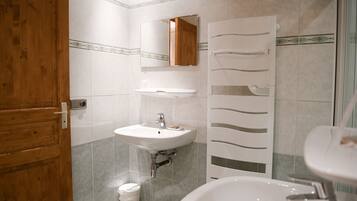 Une salle de bain avec une porte en bois, un lavabo blanc, un miroir et un espace douche.
