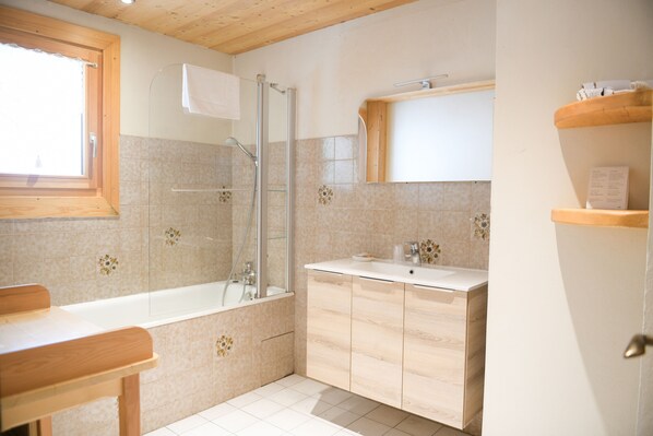 Un baño moderno con ducha envuelta en vidrio, tocador de madera y un espejo grande sobre el lavabo.