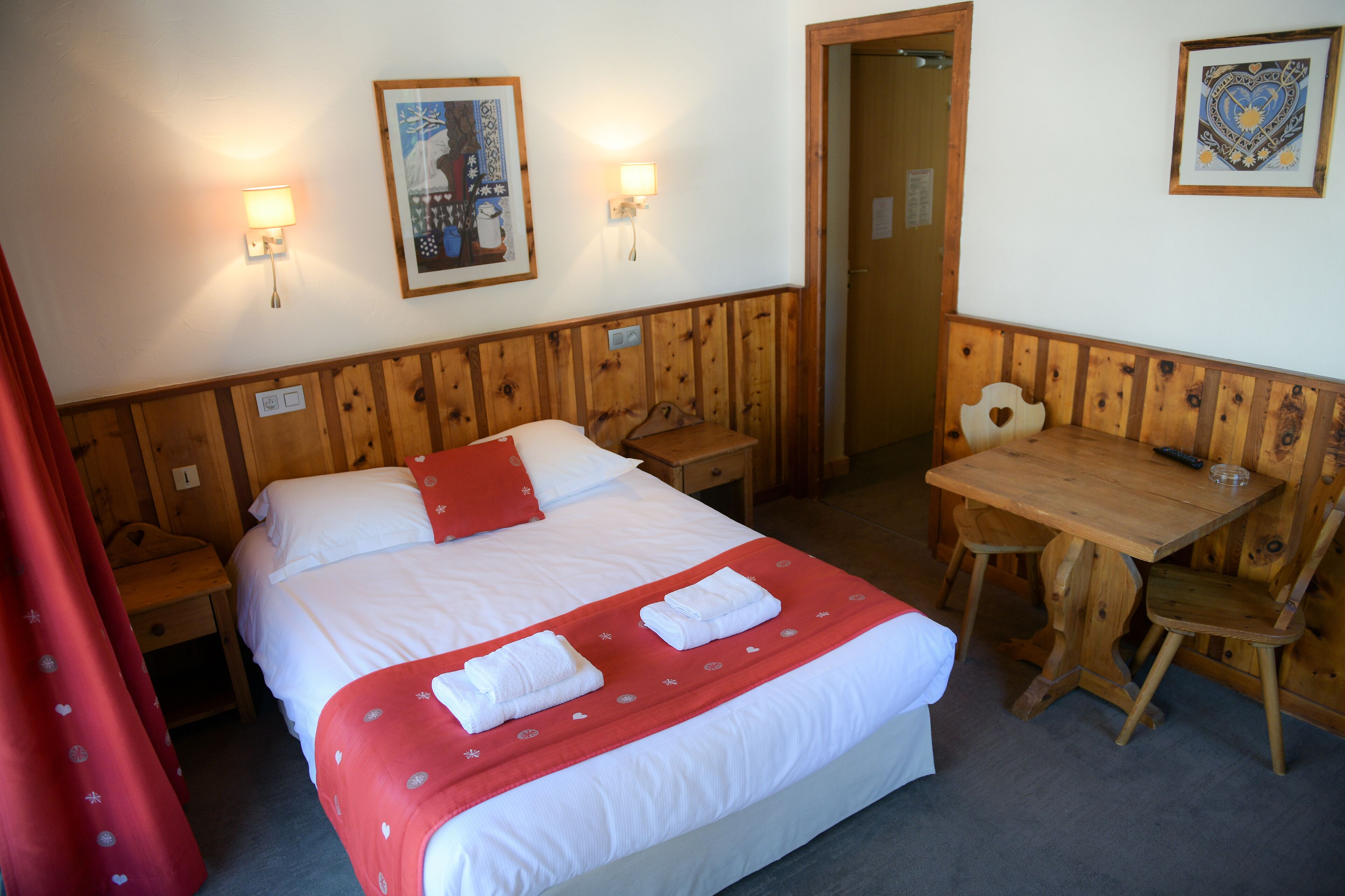 Una habitación de hotel con una cama, una mesa de madera y dos lámparas fijadas a la pared.