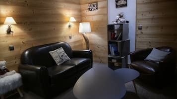 Una habitació acollidora amb un sofà de pell negra, una taula rodona petita i una prestatgeria.