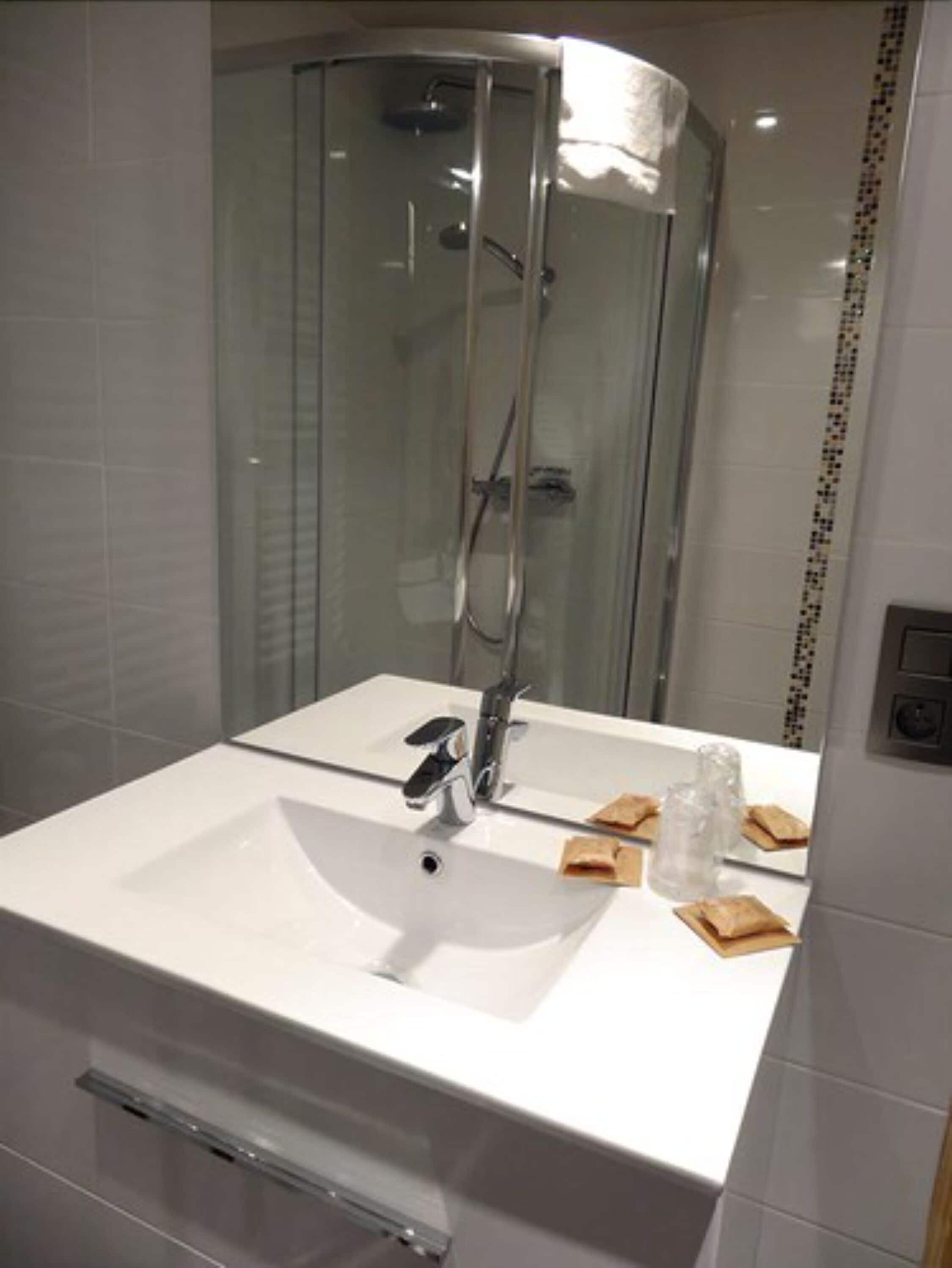 Une salle de bain moderne avec un lavabo blanc, un miroir et une douche à parois de verre.