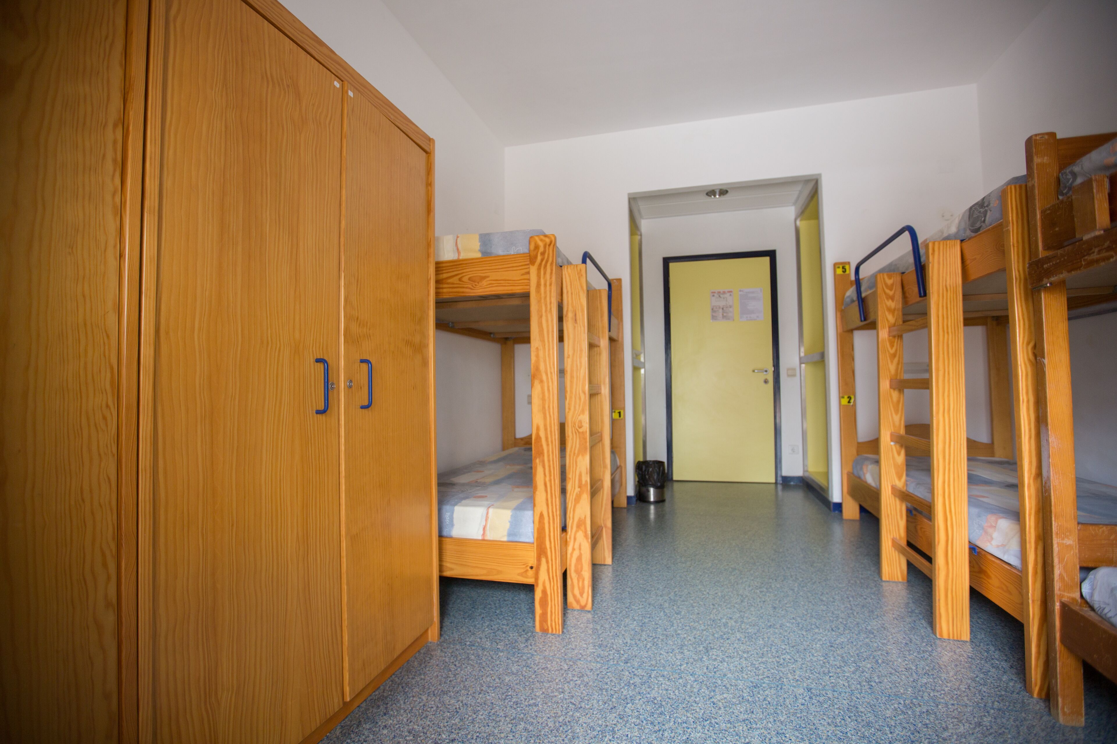 A dormitory room with bunk beds, wooden wardrobes, and a door leading to another room.