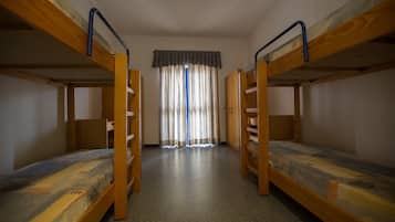 Quarto com duas beliches, janela com cortinas e piso coberto por carpete.