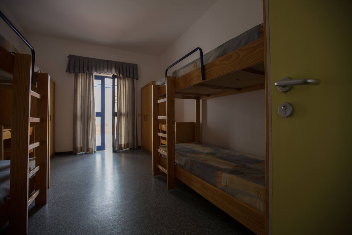 A dormitory room with bunk beds, a door, and a window with curtains.