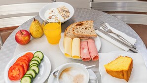 A breakfast setting with a plate of sliced tomatoes, cucumbers, a glass of orange juice, a plate of ham and cheese, a slice of cake, and a cup of coffee. - HI Beja - Pousada de Juventude - Hostel (Beja)