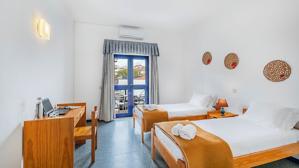 A hotel room with a desk, two beds, a view through a blue door, and decorative wall art. - HI Beja - Pousada de Juventude - Hostel (Beja)