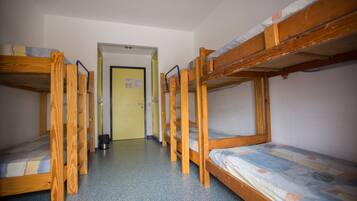 Un dormitorio con literas dispuestas en fila, una puerta en el centro y un cubo de basura cerca de la puerta.