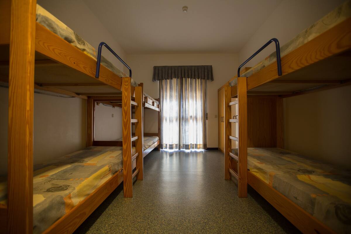 A room with three bunk beds aligned in a row, a window with curtains, and a door in the background.