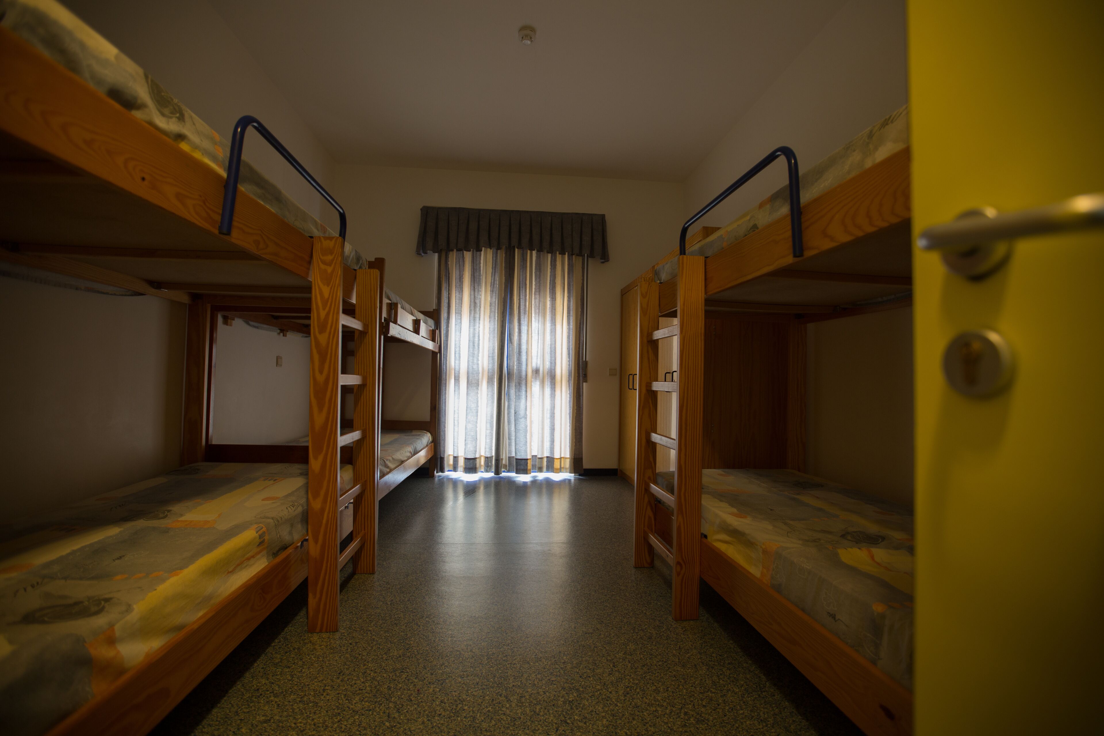 Una camera del dormitorio con letti a castello, una finestra con tende e una porta.