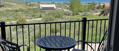 A balcony with two chairs and a table, overlooking a scenic view of a lake and distant mountains.