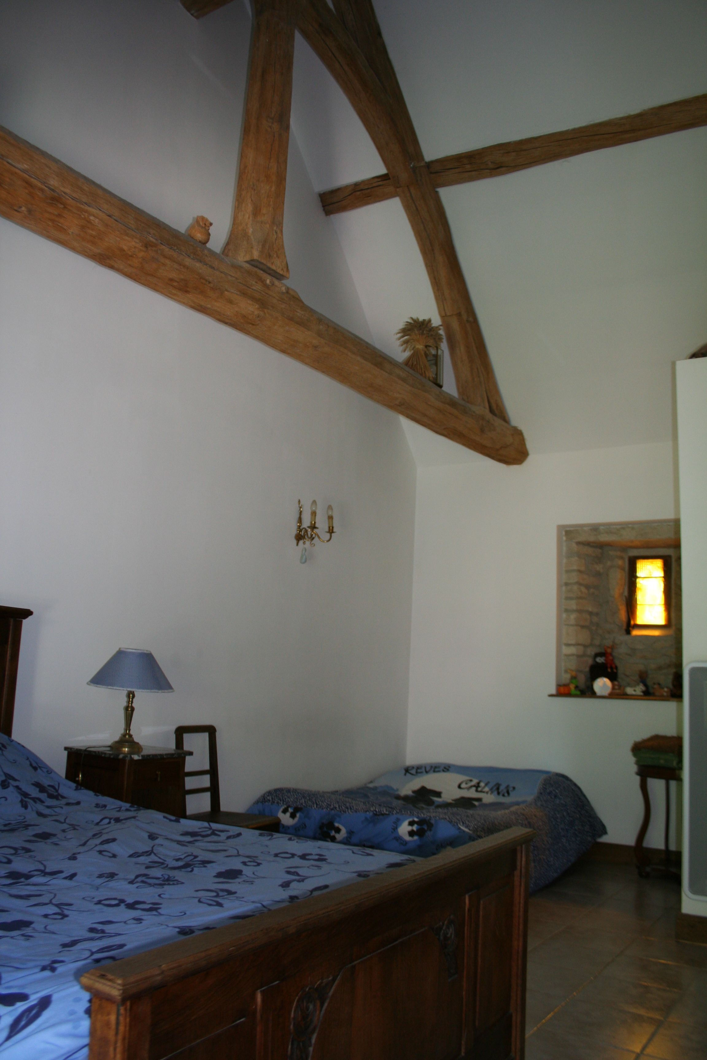 A bedroom with a wooden bed, a nightstand, a lamp, a dresser, and a stone fireplace.