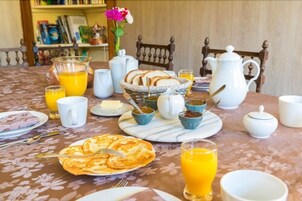 Una mesa de desayuno con diversos alimentos, como panqueques, jugo de naranja y una jarrón de jugo.