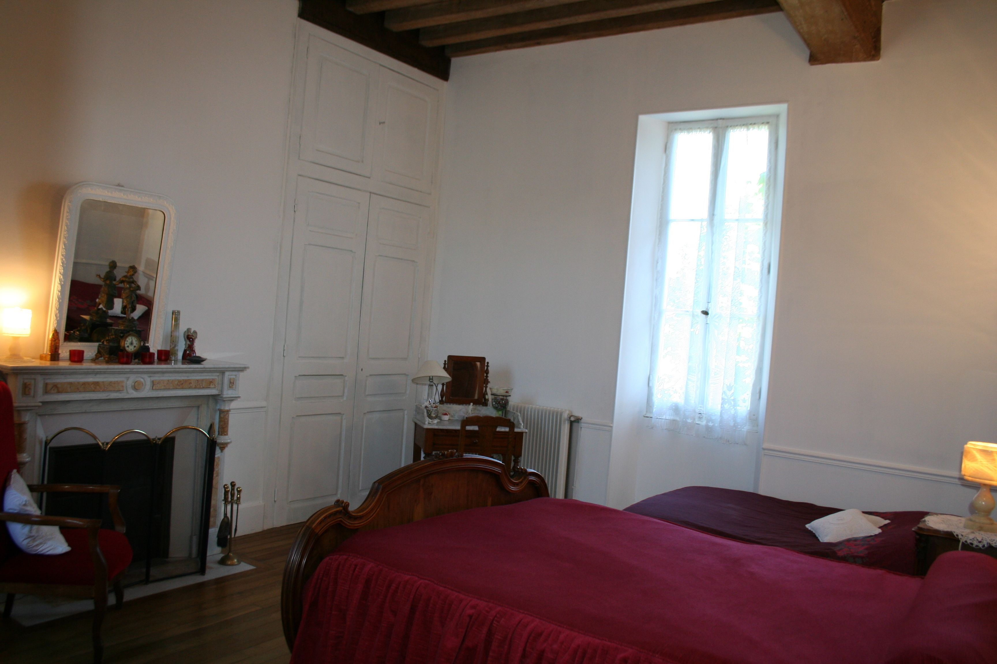 Un dormitorio con cama, cómoda, espejo, chimenea y ventana.