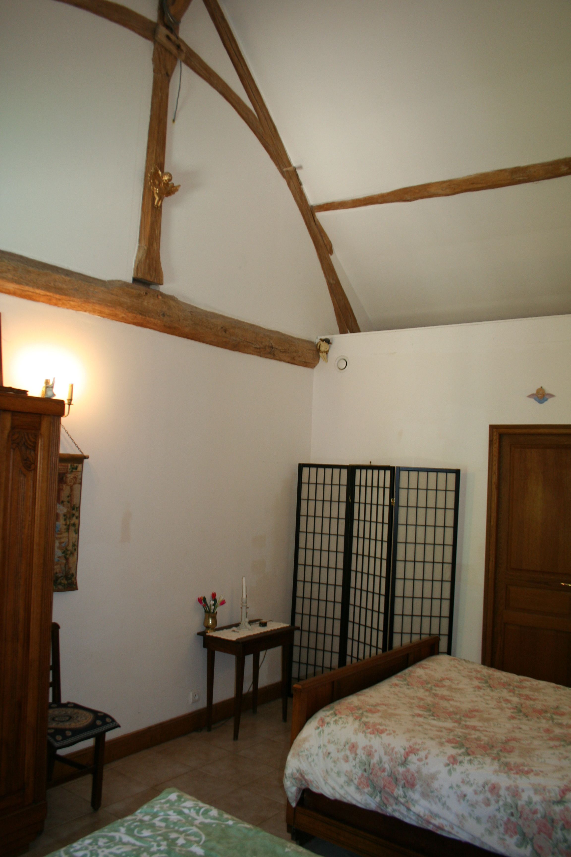 A bedroom with a wooden bed, a nightstand, a chair, a small table with a lamp, and a decorative screen.
