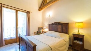 Een slaapkamer met een houten bed, een nachtkastje met een lamp, een stoel en een raam met gordijnen.