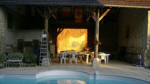 Een zwembadgedeelte met een overdekt terras, tuinmeubels en een ladder naar een hoger niveau.