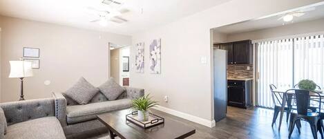 A modern living room with a gray sofa, a coffee table, and a dining area with chairs and a table.