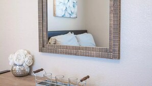 A mirror with a textured frame on a wall, a vase with white flowers, and a tray with glasses and a corkscrew.