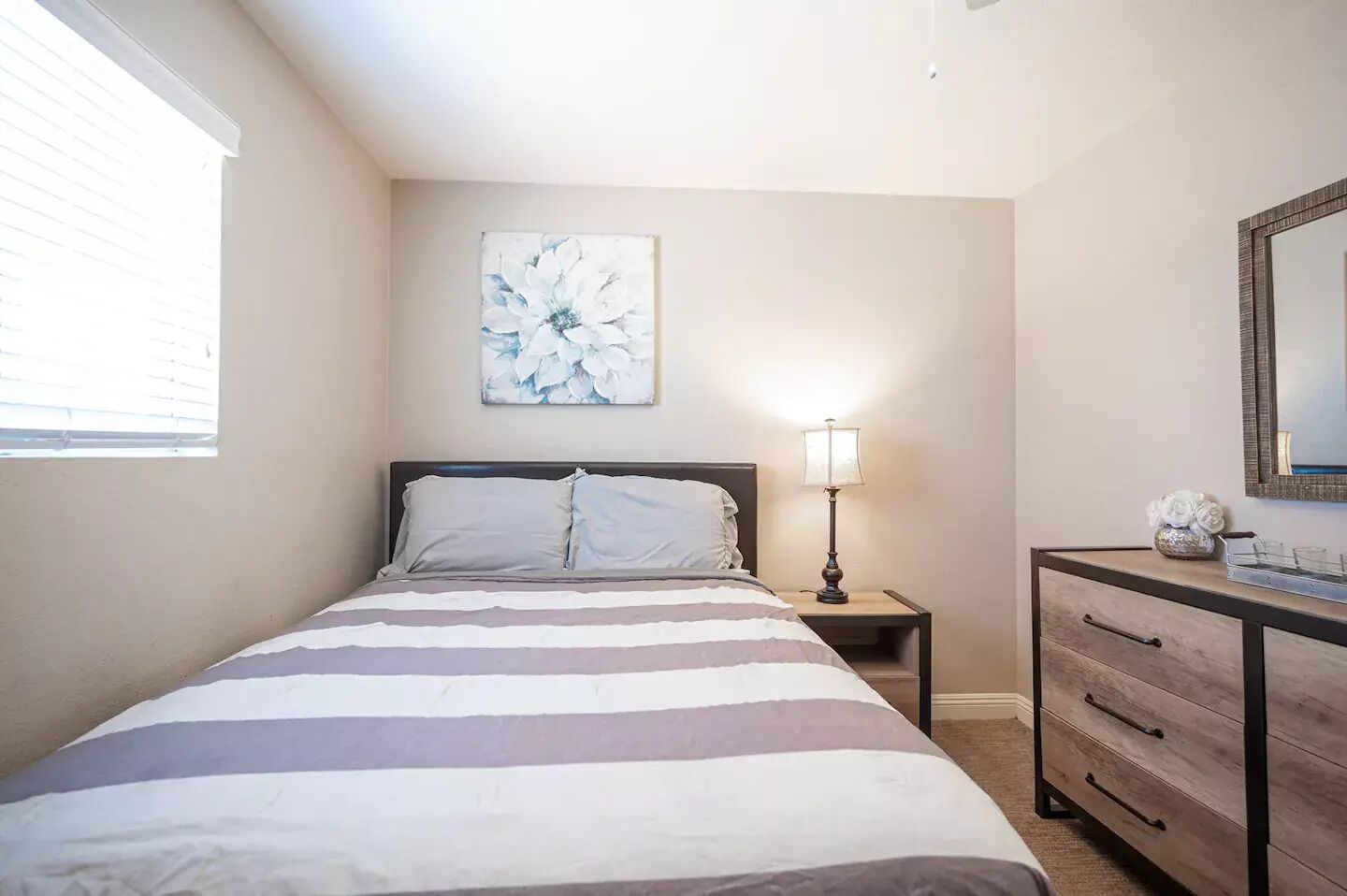 Une chambre à coucher comprenant un lit, une table de chevet, une commode, une lampe et un miroir fixé au mur.