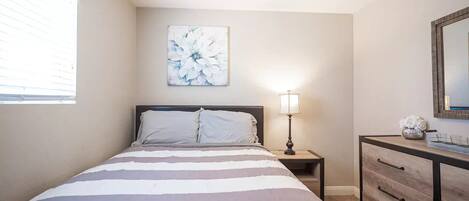 Une chambre à coucher comprenant un lit, une table de chevet, une commode, une lampe et un miroir fixé au mur.