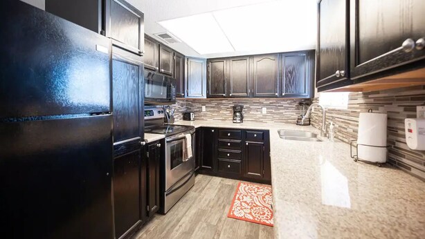 A modern kitchen with dark cabinetry, stainless steel appliances, a granite countertop, and a patterned rug.