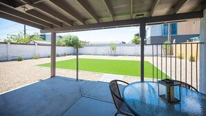 A covered patio with a table and chairs, a small lawn, and a view of a residential area.